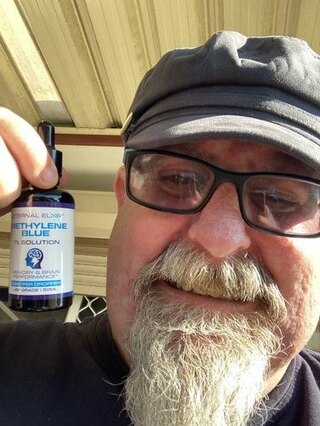 Person wearing glasses and a cap holding an Eternal Elixir bottle